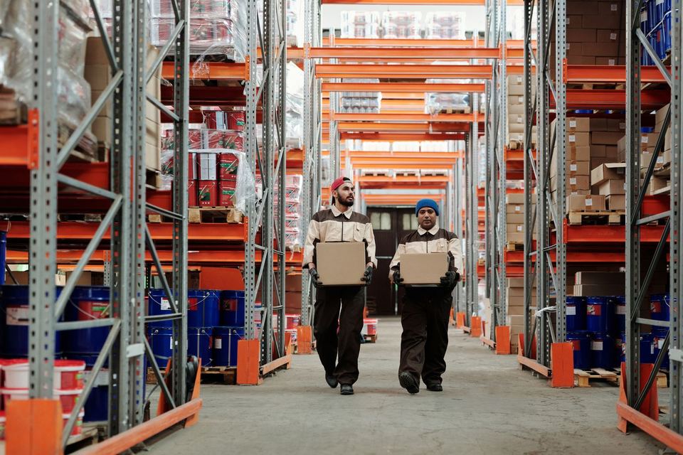 Two warehouse workers carrying parcels down an aisle
